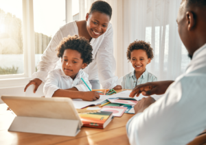 Two adults teaching financial literacy to two school-aged children sitting at a table with a tablet surrounded by learning materials