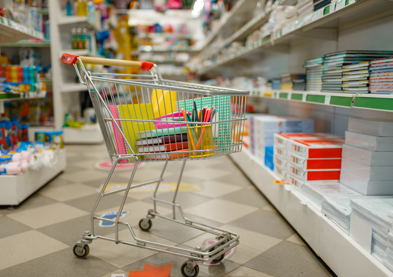 A shopping cart filled with school supplies placed in a store aisle full of books and other supplies