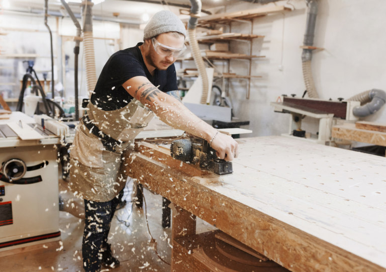 Woodworker wearing a cap and safety glasses using a saw to cut wood